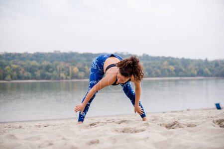Photo for Young female athlete stretching on beach. - Royalty Free Image