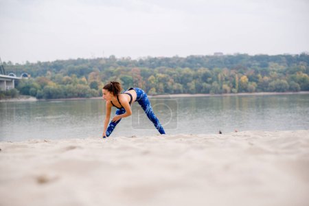 Photo for Young woman stretching on the beach, finishing her sports training. - Royalty Free Image