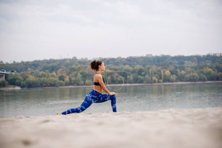 Photo for Young woman stretching her legs on sand, warmin up. - Royalty Free Image