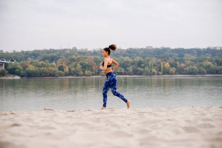Photo for Young woman jogging on beach, wearing blue jogging pants and barefoot. - Royalty Free Image