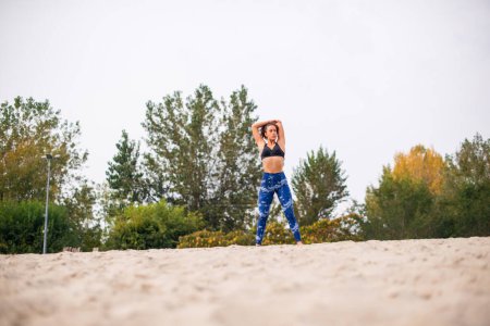 Photo for Young woman doing stretching exercises in the nature, looking away. - Royalty Free Image