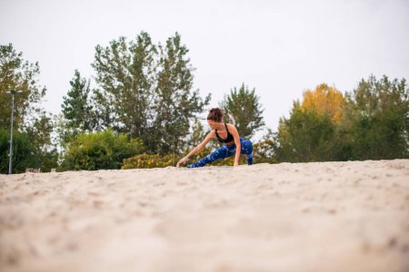 Photo for Woman warming up on the beach, stretching her legs. - Royalty Free Image