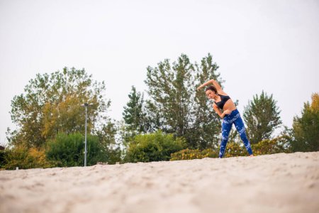 Photo for Caucasian woman exercising outdoors, standing in the sand. - Royalty Free Image