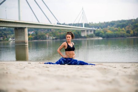 Photo for Smiling woman doing yoga on the beach, looking away. - Royalty Free Image