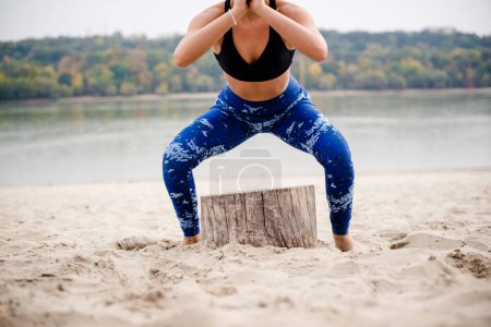 Photo for Woman doing squats on the beach, mid section. - Royalty Free Image