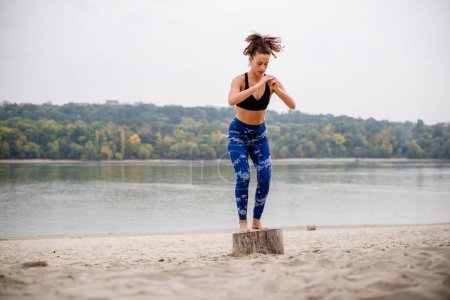 Photo for Female athlete exercsising on the beach, jumping on the stump and down. - Royalty Free Image