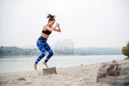 Photo for Side view of woman jumping on the beach, on the wooden stump, horizon over water in background. - Royalty Free Image