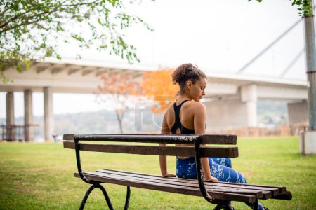 Photo for Rear view of young woman sitting on park bench, preparing for next exercise. - Royalty Free Image