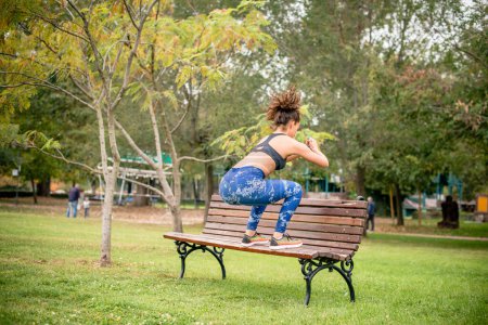 Female athlete doing squats on park bench, rear view.