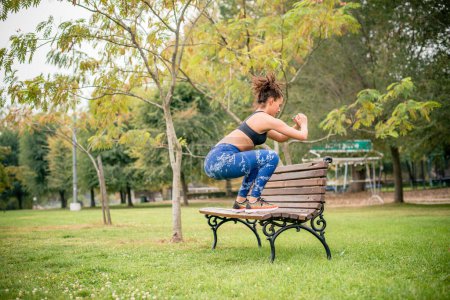 Photo for Female athlete standing on park bench, doing exercising. - Royalty Free Image