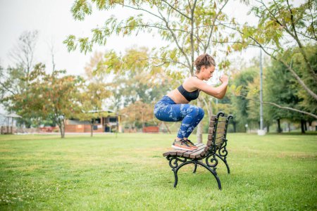 Photo for Caucasian athlete doing squats on park bench. - Royalty Free Image