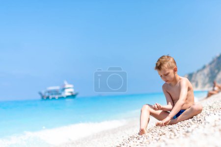 A boy is playing with pebbles on the beautiful, pebbly beach by the turquoise water