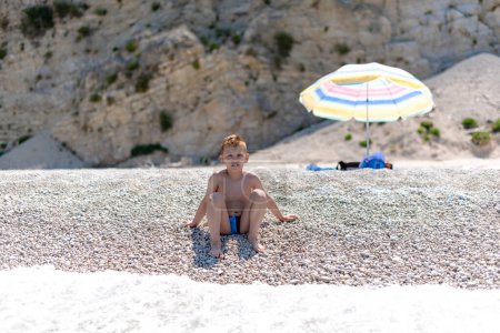 Un niño está sentado en la playa de guijarros