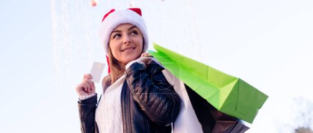 Téléchargez les photos : Portrait de femme dans le chapeau Santa tenant sac à provisions, et carte de crédit. - en image libre de droit