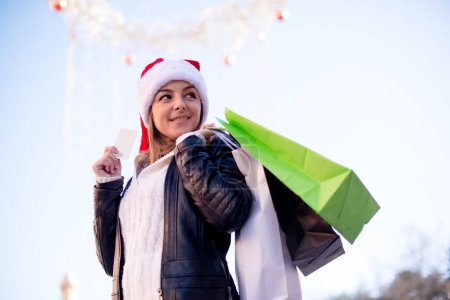 Téléchargez les photos : Fille de Noël avec des sacs shoppinh et carte de crédit, souriant et regardant par-dessus l'épaule. - en image libre de droit