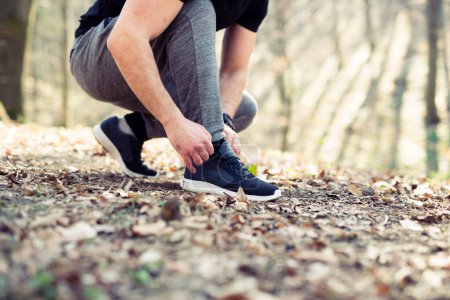 Téléchargez les photos : Coureur attachant ses chaussures se préparant pour un jogging, herbe - en image libre de droit