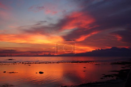 Téléchargez les photos : Wonderful Sunset in the Philippines with red and yellow clouds at the sky and some rocks in the ocean with reflection. High quality photo - en image libre de droit
