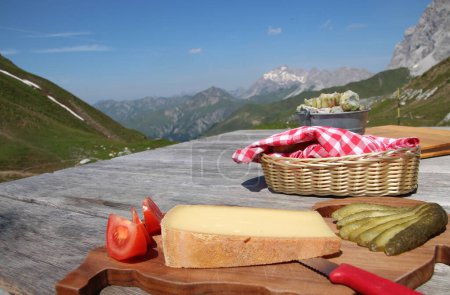 Teller mit Käse, Essiggurken und Tomaten und eine Schüssel Brot mit schönem Bergblick im Hintergrund. Die Schweiz. Swiss-Plate vorhanden. Hochwertiges Foto