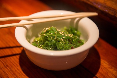 Foto de Ensalada de algas con palillos servidos en un bar de sushi - Imagen libre de derechos