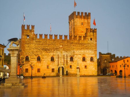 Téléchargez les photos : Imposant château médiéval encore en parfait état sur la place de Marostica. carré célèbre pour le jeu d'échecs. Architecture historique éclairée par des lumières un soir d'été.Il y a aussi des drapeaux et des sculptures comme dans le lion de San Marco - en image libre de droit