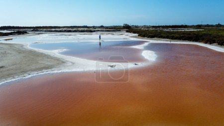 man walking barefoot in a salt strip surrounded by salty pink water. tourist point in Provence in the Camargue Regional Natural Park where the salin de giraud are located. Stage of a trip to France in the midst of nature. tranquility and carefreeness