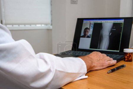 Téléchargez les photos : Rendez-vous chez le médecin. Consultant travaillant sur ordinateur portable. Radiographie d'un patient à l'écran de l'ordinateur lors d'un chat à distance avec DR à l'hôpital ou à la clinique. Focus sur le clavier. - en image libre de droit