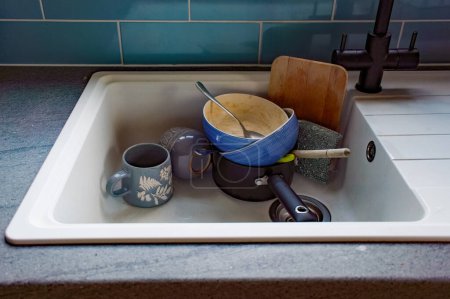 Téléchargez les photos : Évier de vaisselle sale en attente d'être lavé, tasses, casserole, bols et cuillères après la vaisselle du petit déjeuner. éditorial, documentaire. - en image libre de droit