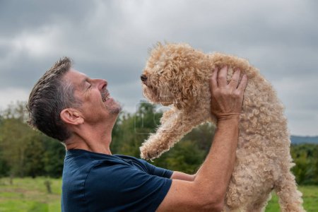 Photo for Man with his dog hugging and playing outdoor in the park. Toy poodle. Friendship and love concept. copy space. - Royalty Free Image