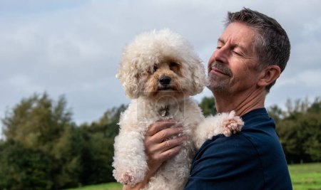 Photo for A man hugs his Bichon Frise dog in the park. Happy man and dog love and friendship concept. - Royalty Free Image