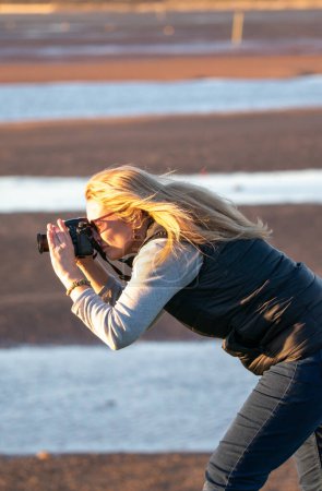 Téléchargez les photos : Photographe, dame d'âge moyen capturant des photos à la plage à l'heure d'or. coup franc. - en image libre de droit