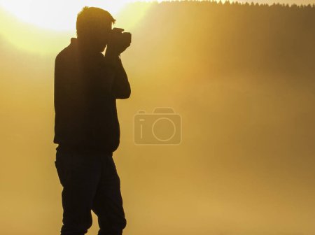 Téléchargez les photos : Un photographe masculin se tient debout en plein soleil doré pour prendre une photo. espace de copie. - en image libre de droit