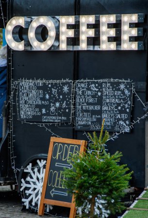 Téléchargez les photos : Café dans un marché de Noël. Fond noir avec de grandes lumières blanches illuminées annonçant des thés chauds et des boissons au café à vendre auprès d'un vendeur indépendant sur une place du marché. - en image libre de droit