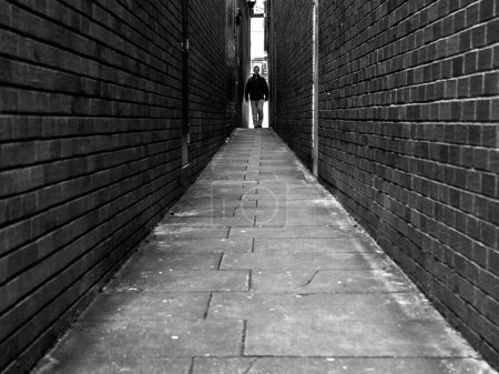 Une ruelle urbaine en briques étroites. Une passerelle texturée et contrastée qui s'amenuise jusqu'à disparaître. capture monochrome. Un homme se tient au bout de l'allée. 