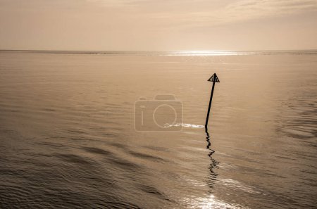 Calm and relaxing seascape with reflective still waters in low amber light, a relaxing meditative peaceful scene. Navigation marker in silhouette. Copy space.