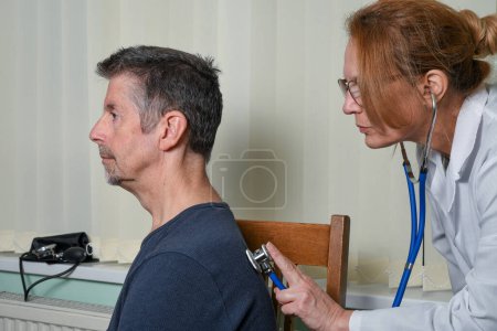Docteur examinant un patient à un rendez-vous. Un médecin généraliste féminin portant un manteau blanc vérifie les poumons de sa patiente pour déceler des crépitements avec un stéthoscope tout en discutant du traitement à l'hôpital ou à la clinique.