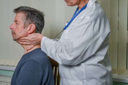 Doctor examining a patient at an appointment. A female GP wearing a white coat checks her patient's swollen glands whilst discussing the treatment at a hospital or clinic.