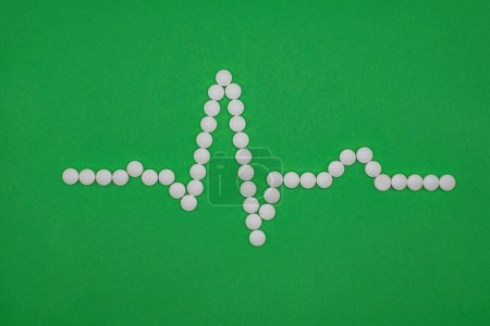 Photo for ECG wave form made of medical pills against a green background. PQRST sinus rhythm shape formed from white tablets. Clinical image editorial medical heart related picture. EKG cardiac trace. - Royalty Free Image