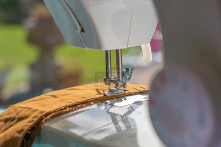 Photo for Sewing machine foot in Selective focus with the control knob in soft focus. The needle is about to sew a brown fabric. - Royalty Free Image