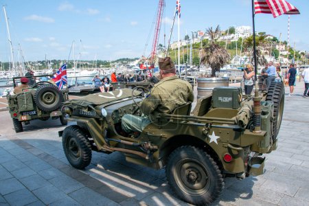Foto de Torquay, Devon, Reino Unido. 06-06-23. Dos Jeeps Willies de la Segunda Guerra Mundial en el puerto de Torquay. Un jeep lleva una bandera de estrellas y rayas americanas, y el otro una bandera de Union Jack. V Día E. - Imagen libre de derechos