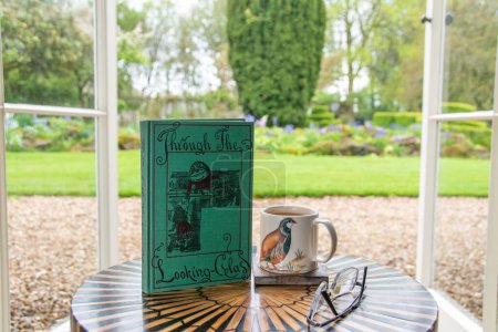 Photo for Ideford, Devon, uk. April 15th 2023. Through the looking glass, by Lewis Carroll. The picture is set against a softly focused garden background. Selective focus on the front cover. Classic book - Royalty Free Image