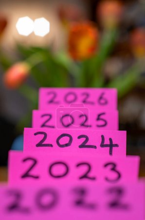 Photo for The year 2024 in sharp text on pink with the years 2022 to 2026 in soft focus. Highlighting the change of year. Soft flowery bokeh background. New year calendar image. Celebration and upbeat theme - Royalty Free Image