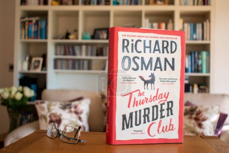 Photo for Ideford, Devon, uk. April 15th 2023. The Thursday murder club, by Richard Osman. The picture is set against a softly focused bookcase background. Selective focus on the cover of the book. - Royalty Free Image