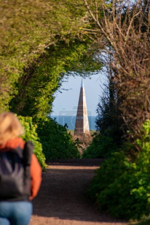 Photo for Exmouth, Devon, uk. April 3rd 2023. Exmouth Geoneedle as seen from a public footpath. Selective focus on the Geoneedle. A lady walks along the path towards the Geoneedle adding interest and scale - Royalty Free Image
