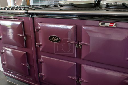 Photo for Ottery, Devon, uk. March 25th 2023.  Aga range cooker in plum color. Country kitchen range oven in close up. Aga logo on the front. Iconic stove in an English farmhouse kitchen. Food preparation. - Royalty Free Image