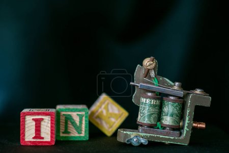 Photo for Churston, devon, uk. December 17th 2022. Tattoo gun with selective focus on the word American. Wooden letter blocks say the word Skin in softer declining focus. Body art image. Tattoo artist. - Royalty Free Image