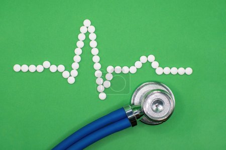 Photo for ECG wave form made of medical pills against a green background. A stethoscope sits below the heart trace measuring the Sinus rhythm. Clinical editorial image. EKG Cardiac trace and a healthy heart - Royalty Free Image
