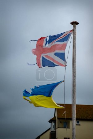 Téléchargez les photos : Drapeau Union Jack déchiré et tatty et drapeau ukrainien battent ensemble. Déchirés et usés, ils volent ensemble dans l'unité. Symbolique d'adversité et de résistance. Drapeaux colorés ensemble. Amis et alliés - en image libre de droit