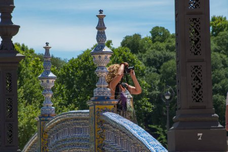 Téléchargez les photos : Séville, Espagne. 8 juin 2022. Une femme tenant un appareil photo reflex numérique prend une photo sur un pont carrelé pittoresque. Soleil brillant avec des couleurs vives. Plein d'intérêt et de composition équilibrée. Éditorial exceptionnel. - en image libre de droit