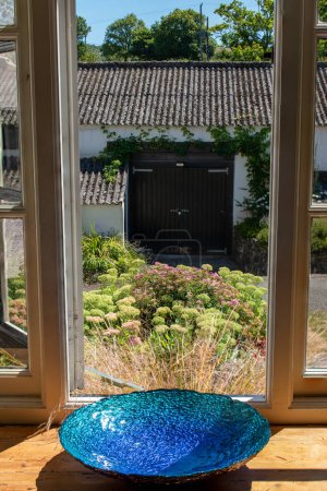 Photo for Beautiful blue bowl sits in a farmhouse window. Looking out across colorful flowers and a country view. A rural barn behind. Outstanding editorial image. Countryside life and idyllic lifestyle. - Royalty Free Image
