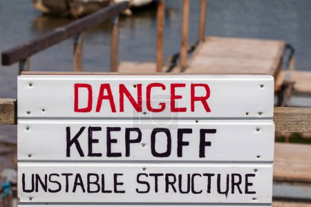 Téléchargez les photos : Danger éloigner signe de structure instable avec passerelle en bois doucement concentré menant à l'eau et les bateaux derrière. - en image libre de droit